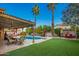 Relaxing backyard featuring a pool, pergola-covered patio, palm trees, and lush green turf at 3473 E Wyatt Way, Gilbert, AZ 85297