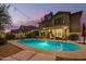 A backyard pool is surrounded by lounge chairs and illuminated by string lights and a covered patio at dusk at 3473 E Wyatt Way, Gilbert, AZ 85297