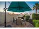 An outdoor dining set with an umbrella provides shade on a brick patio, surrounded by green foliage at 15149 W Vale Dr, Goodyear, AZ 85395