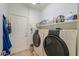 Functional laundry room with washer, dryer, storage shelves, and access door at 40314 W Marion May Ln, Maricopa, AZ 85138