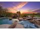 Stunning pool and spa featuring rock waterfalls and lush desert landscaping at sunset at 10596 E Yearling Dr, Scottsdale, AZ 85255