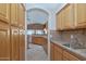 Galley kitchen featuring wood cabinetry, tile backsplash, and stainless steel sink beneath an archway leading to another room at 17806 N Becke Ln, Surprise, AZ 85374