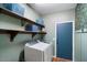 Bright laundry room with blue door and shelving above washer and dryer at 18237 W Port Au Prince Ln, Surprise, AZ 85388