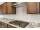Gas stovetop on light granite counters with overhead stainless range hood and dark wood cabinets at 26942 W Renee Dr, Buckeye, AZ 85396