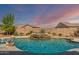 An in-ground pool features a rock waterfall feature, spa, and desert landscaping under a vivid sunset at 18120 W Cassia Way, Goodyear, AZ 85338