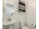 Cozy half bath with pedestal sink, round mirror, and sleek gray cabinet above the toilet at 10134 E Supernova Dr, Mesa, AZ 85212