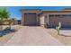 A three-car garage boasts neutral paint, desert landscaping, and a brick driveway under a cloudless sky at 18159 W Piro St, Goodyear, AZ 85338
