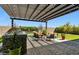 Outdoor kitchen and dining area with a stone grill, covered pergola, and comfortable seating arrangement in the backyard at 22743 N 97Th Dr, Peoria, AZ 85383