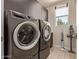 Modern laundry room with gray front-loading washer and dryer, storage, and natural light from a window at 340 E Osborn Rd # 3, Phoenix, AZ 85012