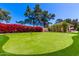 Bright, level artificial putting green accented with red flowers and mature shade trees under a clear blue sky at 87 Biltmore Est, Phoenix, AZ 85016