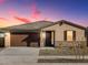 Single-story home at dusk featuring a brown garage door, rock facade, and desert landscaping at 16076 W Prickly Pear Trl, Surprise, AZ 85387