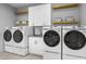 Bright laundry room with four modern appliances, cabinets, and floating shelves with storage baskets at 29599 N 106Th Pl, Scottsdale, AZ 85262
