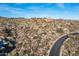 Aerial community view with winding road reveals luxury homes atop a desert hillside, blending architecture with nature at 11130 E Rolling Rock Dr, Scottsdale, AZ 85262