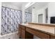 A bathroom with a wide mirror, vanity with brown cabinets, patterned wallpaper, and a shower with a decorative curtain at 12033 W Davis Ln, Avondale, AZ 85323