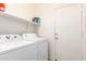 A laundry room with white washer and dryer units and white shelving, next to a white door at 12033 W Davis Ln, Avondale, AZ 85323