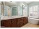 Well-lit bathroom showcasing a dual vanity, large mirror, and soaking tub beneath a window at 11451 E Christmas Cholla Dr, Scottsdale, AZ 85255