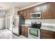 Kitchen featuring stainless steel appliances, wooden cabinetry, light countertop, and door leading to the living room and outside at 9435 S 33Rd Dr, Laveen, AZ 85339