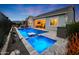Stunning backyard showcasing a modern pool and spa combination, an outdoor kitchen, and lush landscaping under the twilight sky at 20373 W Coolidge St, Buckeye, AZ 85396