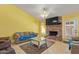 Cozy living room with bright yellow walls, brick fireplace, and tile flooring with large TV above at 1114 W Meseto Ave, Mesa, AZ 85210