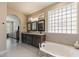 Bathroom featuring a soaking tub, double vanity, arched doorway, and a glass block window at 4932 S Verbena Ave, Gilbert, AZ 85298