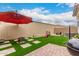 A charming outdoor space with lush artificial grass, a cozy fire pit, and a vibrant red umbrella at 8336 E Idaho Ave, Mesa, AZ 85209