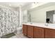 Bright bathroom with double vanity, neutral tile floors, and shower with decorative white and green floral curtain at 8336 E Idaho Ave, Mesa, AZ 85209