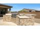 View of stainless steel outdoor gas grill with a stone surround, cabinets, and counter for outdoor kitchen on patio at 20775 W Rattler Rd, Buckeye, AZ 85396