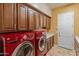 This laundry room features wood cabinets, light countertops, tan walls, and modern, red washer and dryer units at 26473 W Runion Ln, Buckeye, AZ 85396