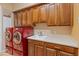This laundry room features red washer and dryer units, wood cabinets, light countertops, and a utility sink at 26473 W Runion Ln, Buckeye, AZ 85396