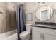 Modern bathroom featuring a round mirror, granite countertop, wood-look tile, and a shower with stylish blue curtain at 8637 E Weldon Ave, Scottsdale, AZ 85251