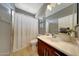 Well-lit bathroom featuring a shower with a white curtain, a cherry wood vanity, and a large mirror at 2850 N 152Nd Ln, Goodyear, AZ 85395