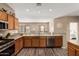 Bright kitchen with granite countertops, wood cabinets, stainless steel dishwasher, and open layout to dining area at 15829 W Boca Raton Rd, Surprise, AZ 85379