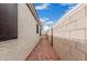 A gravel lined side yard between two beige colored stucco walls with the bright blue sky overhead at 11321 W Austin Thomas Dr, Surprise, AZ 85378