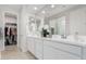 Bright bathroom with double sinks, white cabinets, large mirror, and a doorway to a walk-in closet at 2377 S 245Th Dr, Buckeye, AZ 85326
