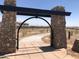 Arched entry with stone pillars, a paved walking path, and desert landscaping in the community at 14594 W Sand Hills Rd, Surprise, AZ 85387