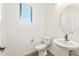 A compact bathroom featuring a pedestal sink, toilet, and a bright window at 27046 W Rockwood Dr, Buckeye, AZ 85396