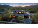 A stunning aerial view of a large, luxurious home featuring a tiled roof, lush landscaping, and mountain views at sunset at 4098 N Golf Dr, Buckeye, AZ 85396