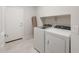 Modern laundry room with white appliances and storage shelving, next to door and rolled carpet at 17758 W Getty Dr, Goodyear, AZ 85338