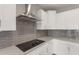 Modern kitchen with sleek cooktop, stainless steel hood, stylish backsplash, and white cabinetry at 4119 S 176Th Dr, Goodyear, AZ 85338