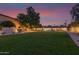 Spacious backyard featuring a lush lawn, mature trees, and an outdoor dining area at dusk at 5960 E Orange Blossom Ln, Phoenix, AZ 85018