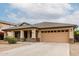Charming home featuring a two-car garage, covered porch with stone accents, and desert landscaping at 16187 W Gibson Ln, Goodyear, AZ 85338