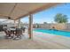 Inviting outdoor pool area with a covered patio, dining set, and lush landscaping at 11540 W Sonoran Ct, Surprise, AZ 85378