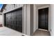 View of a black garage door and front door on a gray home with desert landscaping at 23403 W Albeniz Pl, Buckeye, AZ 85326
