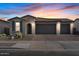 Charming single-story home featuring a three-car garage and desert landscaping under a colorful sky at 22473 E Twilight Dr, Queen Creek, AZ 85142