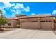 Tan home showcasing desert landscaping, a three-car garage, and a charming tiled roof under a bright blue sky at 1777 W Redfield Rd, Gilbert, AZ 85233