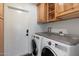 Convenient laundry room with wooden cabinets and a utility sink is equipped with a modern washer and dryer at 10896 N 105Th Way, Scottsdale, AZ 85259