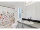 This bathroom features a floral shower curtain, light gray cabinets, and a black faucet at 16643 W Quail Run Rd, Surprise, AZ 85378