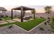 Backyard patio with stylish outdoor seating under a modern pergola, artificial turf, and rock landscaping with mature trees at 19022 W Rose Ln, Waddell, AZ 85355