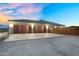 Three-car garage with wooden doors and exterior lighting, framed by a colorful dusk sky at 28204 N Royce Rd, Queen Creek, AZ 85144
