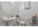 Clean powder room with a pedestal sink, toilet, and decor featuring a modern round mirror and wall art at 10221 W Puget Ave, Peoria, AZ 85345